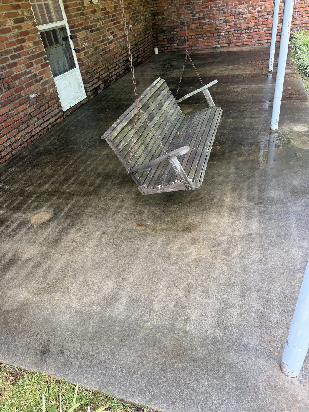 Covered back porch concrete and porch swing before pressure washing, dark mildew stains